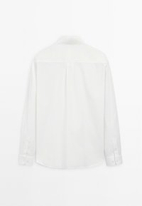 Chemise blanche à manches longues vue de dos, avec un pli central et des poignets boutonnés, sur un fond blanc uni.