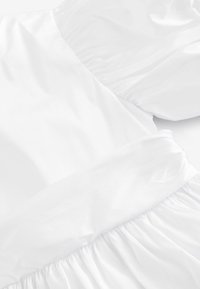 Robe blanche avec un haut lisse et satiné, des manches texturées froncées et une jupe fluide froncée à l'ourlet.