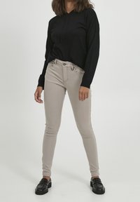 Sudadera negra con mangas largas, vaqueros skinny beige y mocasines negros. Textura suave con un diseño minimalista, ajuste ceñido.