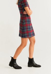 Rot, grün und marineblau karierter Kurzarmkleid mit tailliertem Oberteil und ausgestellt Rock, kombiniert mit schwarzen Leder Stiefeletten mit elastischen Seiten.