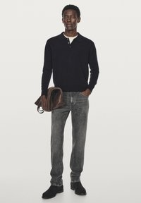 Navy sweater with a collar, gray jeans, and black boots. Brown leather bag held in left arm, slim-fit design, and smooth texture.