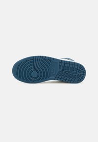 Semelle de chaussure Nike bleue avec motifs de traction circulaires et rectangulaires, logo Nike visible, photographiée de dessous sur fond blanc.