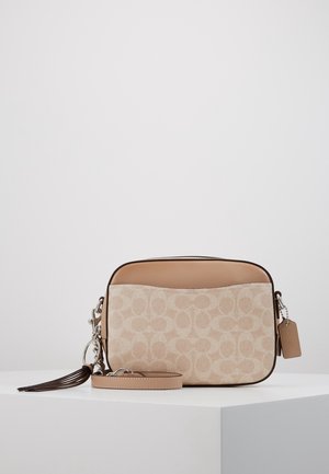 Beige og tan crossbody-taske med signaturmønster, læderkant, aftagelig rem og læderkvast på en hvid piedestal.