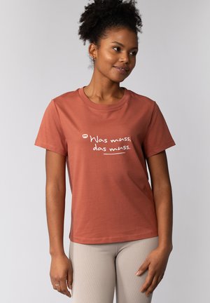 Roestkleurig katoenen t-shirt met korte mouwen en een ronde hals, met witte tekst die zegt "Was muss, das muss." Gladde textuur.
