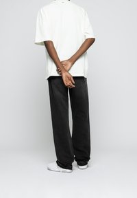 Camiseta de algodón blanca de gran tamaño con mangas cortas, combinada con pantalones vaqueros negros holgados y zapatillas blancas. Fondo neutro.