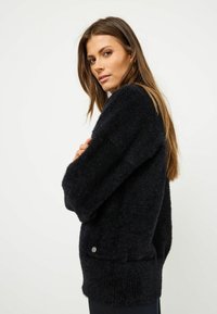 Maglione nero con texture, dal taglio morbido, maniche ampie e una minimale rifinitura in argento vicino all'orlo. Materiale morbido e peloso.