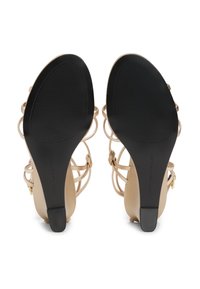 Sandales à talons hauts beiges avec brides, dotées d'une semelle en caoutchouc noir, présentant un design ouvert et des fines sangles pour la ventilation et le soutien.