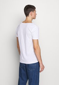 Weißes T-Shirt mit kurzen Ärmeln aus weichem Stoff, mit rundem Halsausschnitt und lockerer Passform, getragen mit blauen Denim-Jeans. Rückansicht.