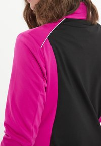 Tætsiddende sportjakke med en lyserød front og en sort ryg, lavet af glat stof med kontrasterende hvide detaljer langs skuldersømmene.
