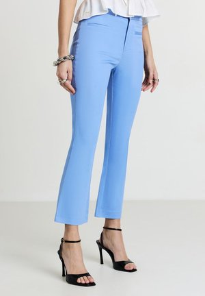 Light blue tailored pants with a slim fit, flat front, and two side pockets, paired with black strap high heels. Smooth texture, cropped length.