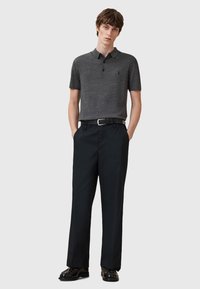 Graues Polohemd mit Kragen und drei Knöpfen, kombiniert mit dunkelblauen Hosen und schwarzen, glänzenden Schuhen.