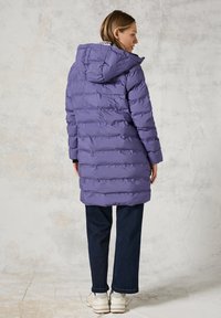 Fialová zateplená bunda s kapucí, s prošívaným vzorem a dlouhými rukávy. V kombinaci s tmavými džíny a světlými teniskami.