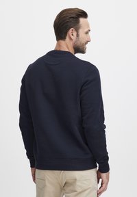 Sudadera azul marino hecha de una mezcla de algodón. Cuenta con un cuello redondo, puños acanalados y una textura suave. Costuras visibles a lo largo de las costuras.