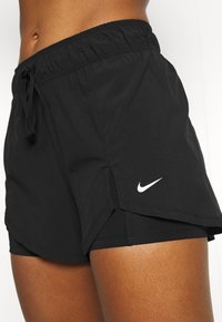 Pantalones cortos deportivos negros con cintura ajustable con cordón, forro interior y aberturas laterales. Presentan un pequeño logo blanco de Nike en el dobladillo inferior.