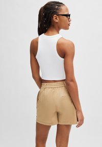 Witte mouwloze crop top gecombineerd met beige shorts met elastische taille. De shorts hebben zijzakken en een achterzakdetail.