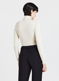 Beige, enganliegender Rollkragenpullover mit langen Ärmeln. Glatte Textur. Kombiniert mit schwarzen, maßgeschneiderten Hosen mit Seitentaschen.