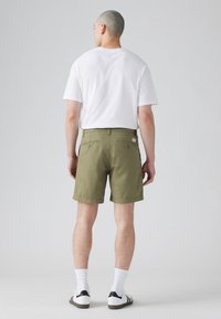Pantaloni scurți verzi măslinii pentru bărbați, cu o croială dreaptă, buzunare la spate, și un tricou alb cu gât rotund, accesorizat cu șosete albe și adidași cu accente negre.