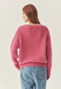 Pulover tricotat roz, cu un croi lejer, tiv ondulat și mâneci largi, asortat cu blugi denim de un albastru deschis, care au detalii cu broderie de flori.