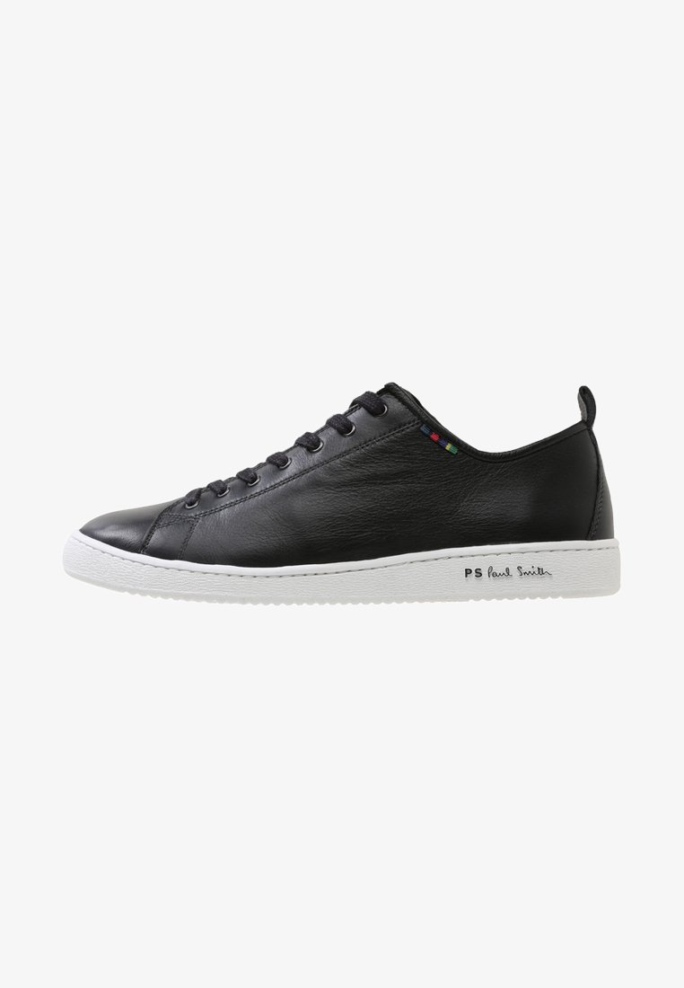 Zapatillas de cuero negro con suela de goma blanca. Presenta puntera redonda, seis ojetes para cordones y un acento multicolor cerca de la lengüeta, logotipo en relieve en el lateral.