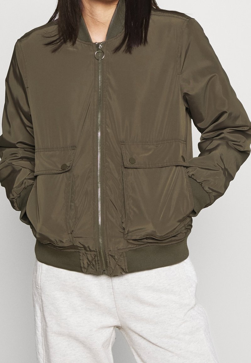 Olivově zelená bomber bunda se zapínáním na zip, žebrovanými manžetami a spodním lemem a dvěma předními kapsami. Hladká textura s minimálním zdobením.