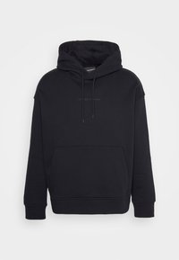 Černá mikina s kapucí a přední kapsou, vyrobená z měkkého materiálu. Má jednoduchý design a decentní logo na hrudi.