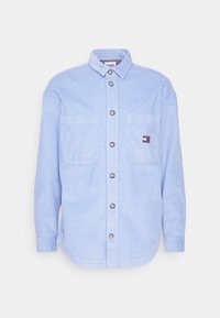 Jasnoniebieska koszula sztruksowa z długimi rękawami, zapinana na guziki z przodu, z dwoma kieszeniami na piersi oraz naszywką z logo. Posiada klasyczny kołnierzyk i fakturowaną tkaninę.