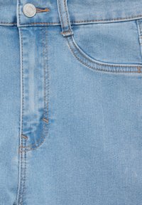 Jean en denim bleu clair avec des coutures visibles, une poche avant et une fermeture à bouton en métal. Le matériau présente une texture lisse avec peu de délavage.