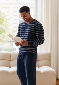Blauw-wit gestreepte lange mouw blouse en donkerblauwe loungebroek, met een relaxte pasvorm. De persoon staat en leest een boek.
