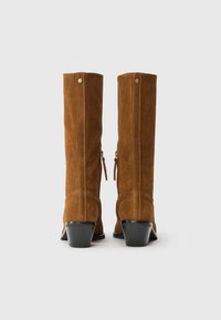 Ψηλές καφέ σουέτ μπότες με κομψό σχεδιασμό, χαρακτηριστικά υφής φινίρισμα, κλείσιμο με φερμουάρ και τριγωνική σόλα.
