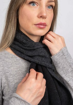 En grå og sort tørklæde draperet om halsen, med et struktureret strikdesign. Materialet ser blødt og varmt ud med lagdelte folder.