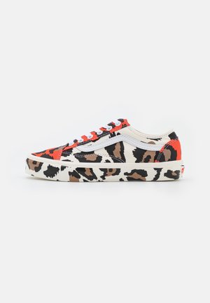 Deportivas bajas con estampado de leopardo, franja lateral blanca, cordones blancos y detalles rojos en el talón y la puntera sobre un fondo blanco.