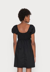 Vestido preto com mangas curtas bufantes, corpete franzido e saia rodada. A parte de trás possui um decote quadrado com uma textura suave.