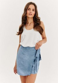Světle modrá zavinovací sukně z texturované látky s detailním vázáním v pase, kombinovaná s bílým bezramínkovým topem. Jednoduchý design, ležérní styl.