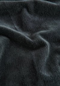 Black corduroy fabric with visible ridges and a soft texture, slightly wrinkled, displaying a deep color and even weave throughout.