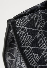 Geantă neagră cu un design geometric. Fabricată dintr-un material texturat, având un trim și un detaliu de închidere negre pentru o prindere sigură.