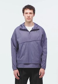 Purple lightweight pullover jacket with a hood, half-zip front, and a front horizontal seam. Features relaxed fit and textured fabric.
