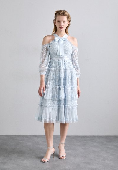 Lyseblå, lagdelt kjole med lace-overlay, gennemsigtige pufærmer, off-shoulder design og satinsløjfe ved halsen. Sammen med sølvhæle.