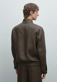 Brun, texturerad jacka med avslappnad passform, med en krage och elastisk nederkant. Knappärmar fulländar designen.