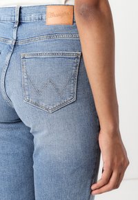 Világoskék farmernadrág klasszikus fazonnal, bőr Wrangler címkével a derékrészen és jellegzetes varrott zseb mintával.