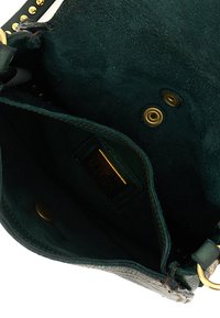 Interno di una borsa in suede verde con hardware dorato, dotata di un'etichetta rettangolare e bottoni a scatto. Texture morbida, forma strutturata, cuciture minime.