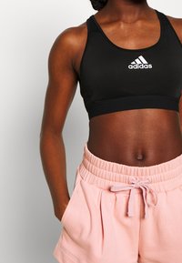 Černá sportovní podprsenka s logem, která má design racerback a elastický pás, spárovaná se světle růžovými sportovními šortkami s páskem na stažení.