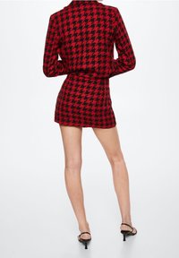 Vestido corto de patrón pata de gallo en rojo y negro, con mangas largas y silueta ajustada, combinado con tacones negros de punta abierta.