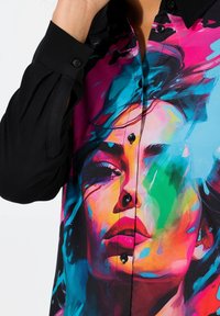 Kleurige blouse met een zwarte kraag en knopen, met een levendig grafisch ontwerp van een gezicht in roze, blauw en groene tinten. Lange mouwen.