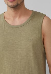 Canottiera senza maniche verde oliva realizzata in tessuto leggero e testurizzato, con scollatura rotonda e un logo ricamato discreto sul petto.