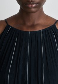 Vestido plissado de cor escura com alças finas, decote franzido e finas riscas brancas a correr verticalmente pelo tecido.