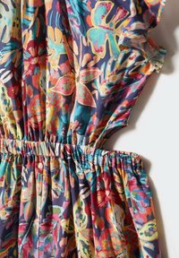 Blommönstrad tyg i livliga färger, med smockad midja och volangärmar. Lättviktsmaterial som andas.