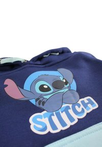 Sweat à capuche bleu marine avec une illustration de Stitch, des accents bleu clair et le texte "STITCH" en police audacieuse et ludique.