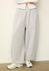 Graue, weit geschnittene Sweatpants aus weichem Stoff mit elastischem Bund. Kombiniert mit weißen Sneakers und einem kurzen weißen Shirt.