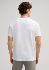 Weißes, lässiges T-Shirt mit Rundhalsausschnitt, kurzen, umgeschlagenen Ärmeln und strukturiertem Stoff. Mit einem kleinen Logotag am unteren Saum.
