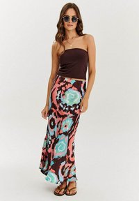 Hnedý top bez ramienok spárovaný s voľnou maxi sukňou s viacfarebným abstraktným vzorom v ružovej, modrej a hnedej farbe. Hnedé ploché sandále.